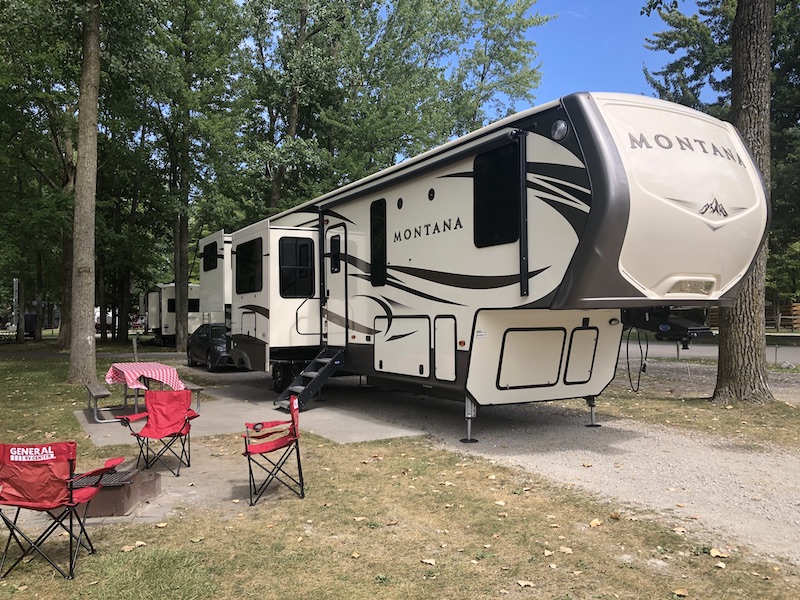 Fifth wheel camper set up with camp chairs nearby.