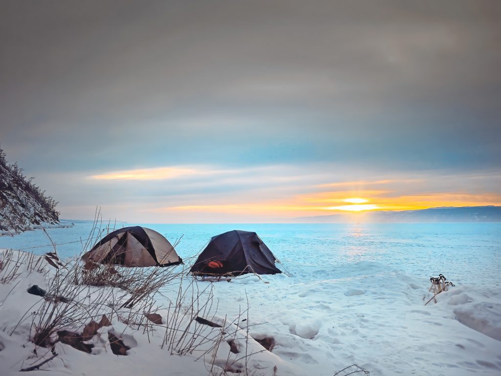 Tents pitched in snow along a lake shore at sunset.